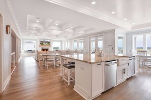 Une cuisine spacieuse dotée d’un grand îlot central, de meubles blancs et offrant une vue sur l’extérieur.