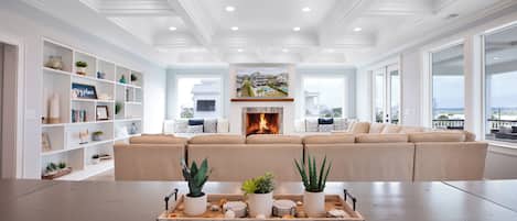 A spacious living room with a large beige sectional sofa, a fireplace, and a view of the ocean.