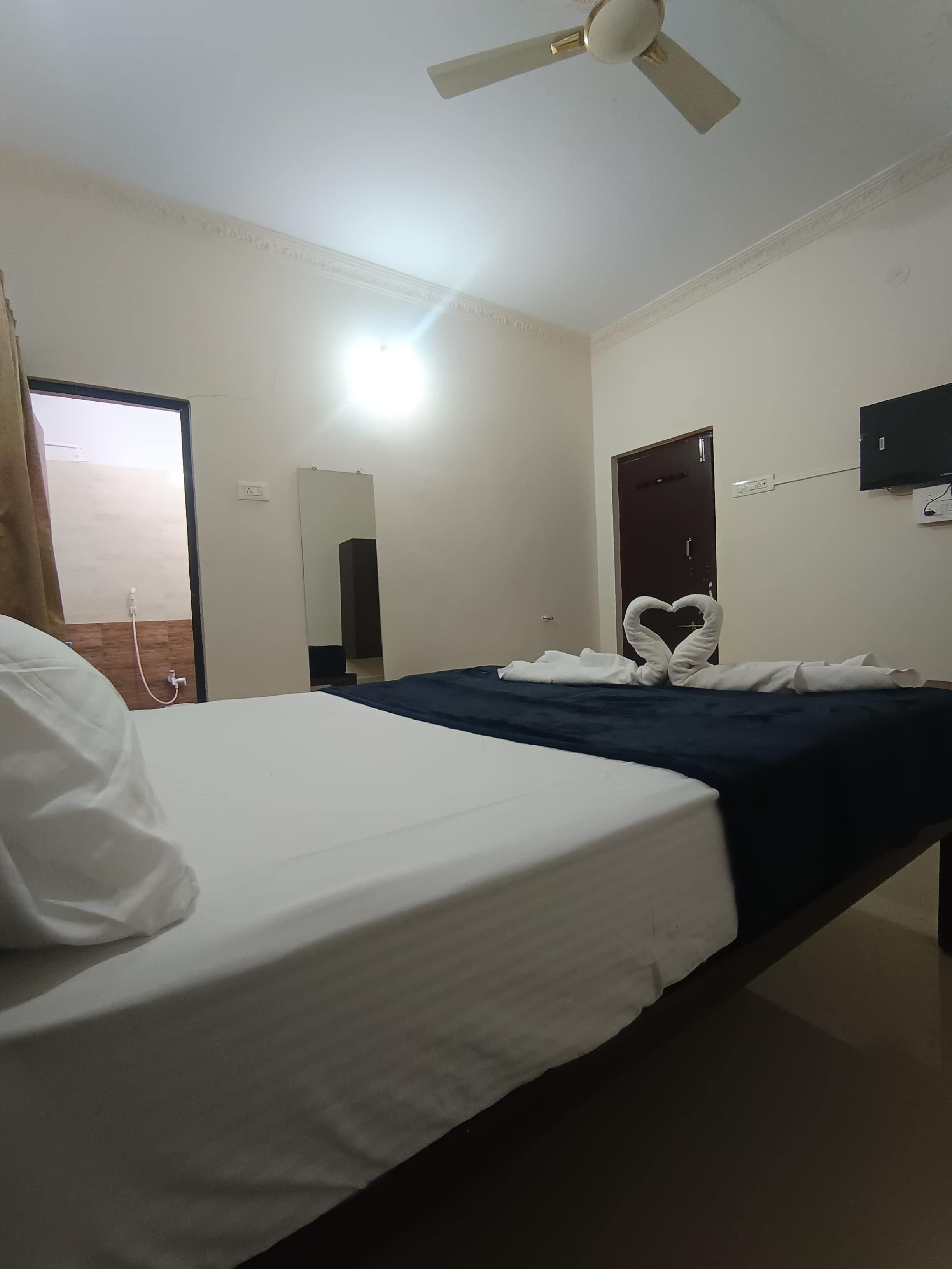 A hotel room with a bed, a ceiling fan, a TV mounted on the wall, and a door.
