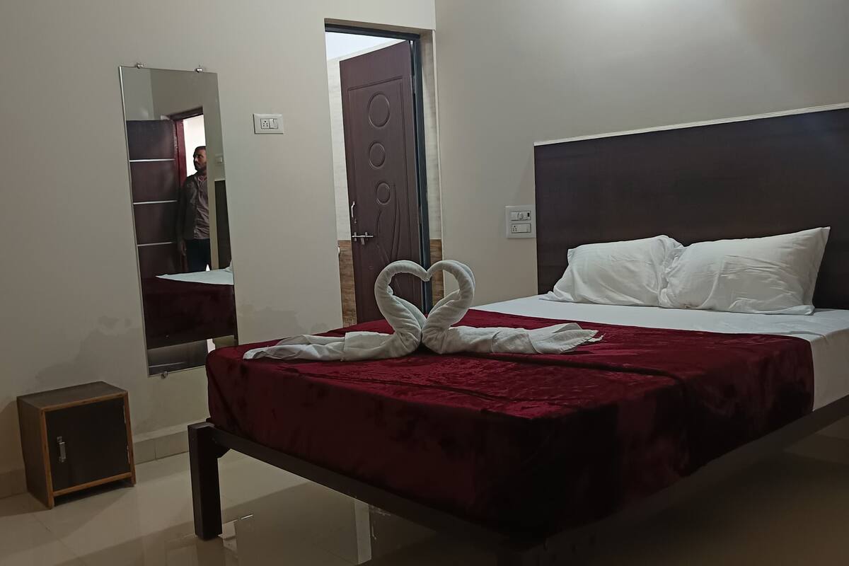 Habitación de hotel con cama, mesita de noche, espejo, puerta y lámpara.