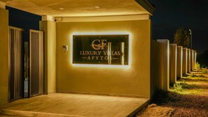 Entrada de uma villa de luxo, com uma placa bem iluminada que diz 'Luxury Villas Afytos'.