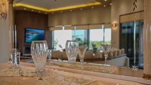 Quarto de hotel com um espelho grande que reflete uma área de refeições, com vários copos de vinho e uma toalha de renda.