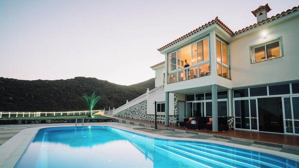 Un edificio moderno de dos plantas con piscina, amplias ventanas y vistas a la montaña.