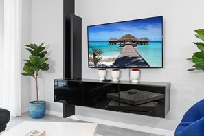 A modern living room with a flat-screen TV mounted on a black entertainment unit, a potted plant, and a remote control on the unit.