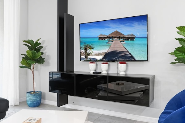 A modern living room with a flat-screen TV mounted on a black entertainment unit, a potted plant, and a remote control on the unit.