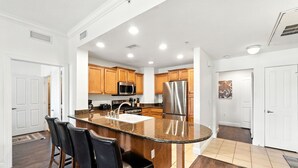 A modern kitchen with granite countertops, stainless steel appliances, wooden cabinets, and a bar area with stools. - Reunion Condo Steps from the Pool! (Kissimmee)