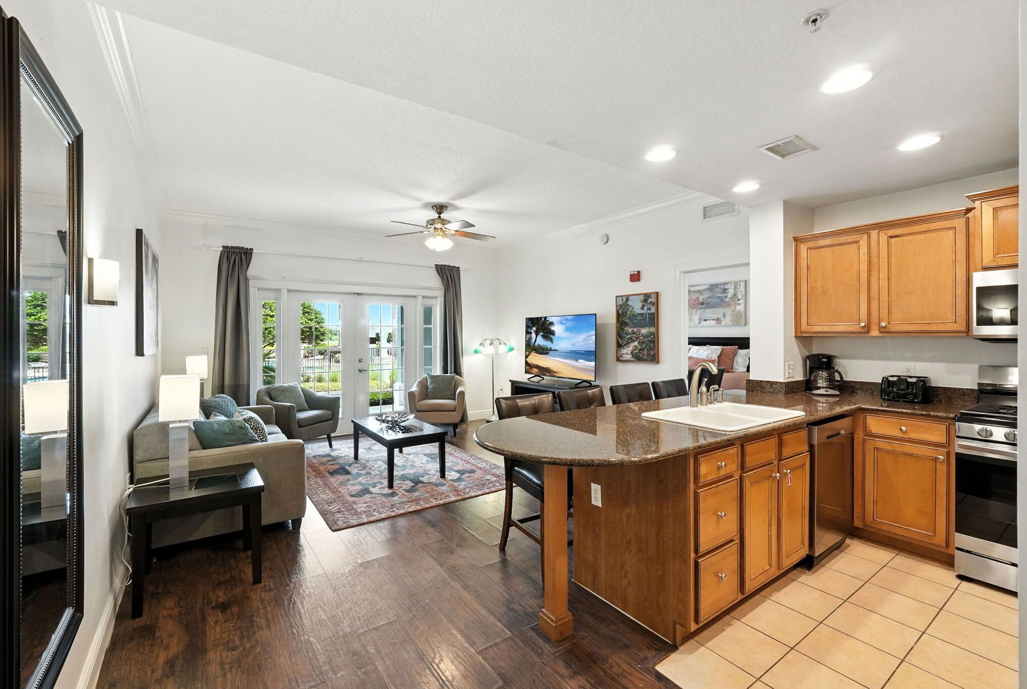 A modern kitchen with wooden cabinets, a granite countertop, and stainless steel appliances. There is a dining area with a table and chairs, and a living room with a sofa and a coffee table. - Reunion Condo Steps from the Pool! (Kissimmee)