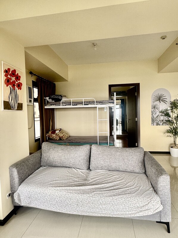 A compact living space with a bunk bed, a sofa, a potted plant, and artwork on the walls. - Levi&Moon's Haven in the Sky 2Bath (Pasay)