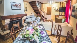 A cozy living room with a fireplace, a dining table set for a meal, a staircase, and a television in the background. - Gîtes chez PAT, a house in the countryside near the beach (Ychoux)
