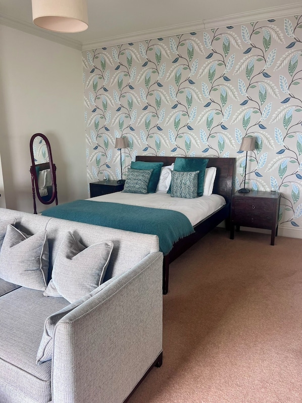 A bedroom with a bed, nightstands, a mirror, and a sofa. - The Hambrough (Ventnor)