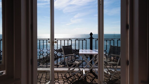 A balcony with a table and chairs, overlooking a body of water and a clear sky. - The Hambrough (Ventnor)
