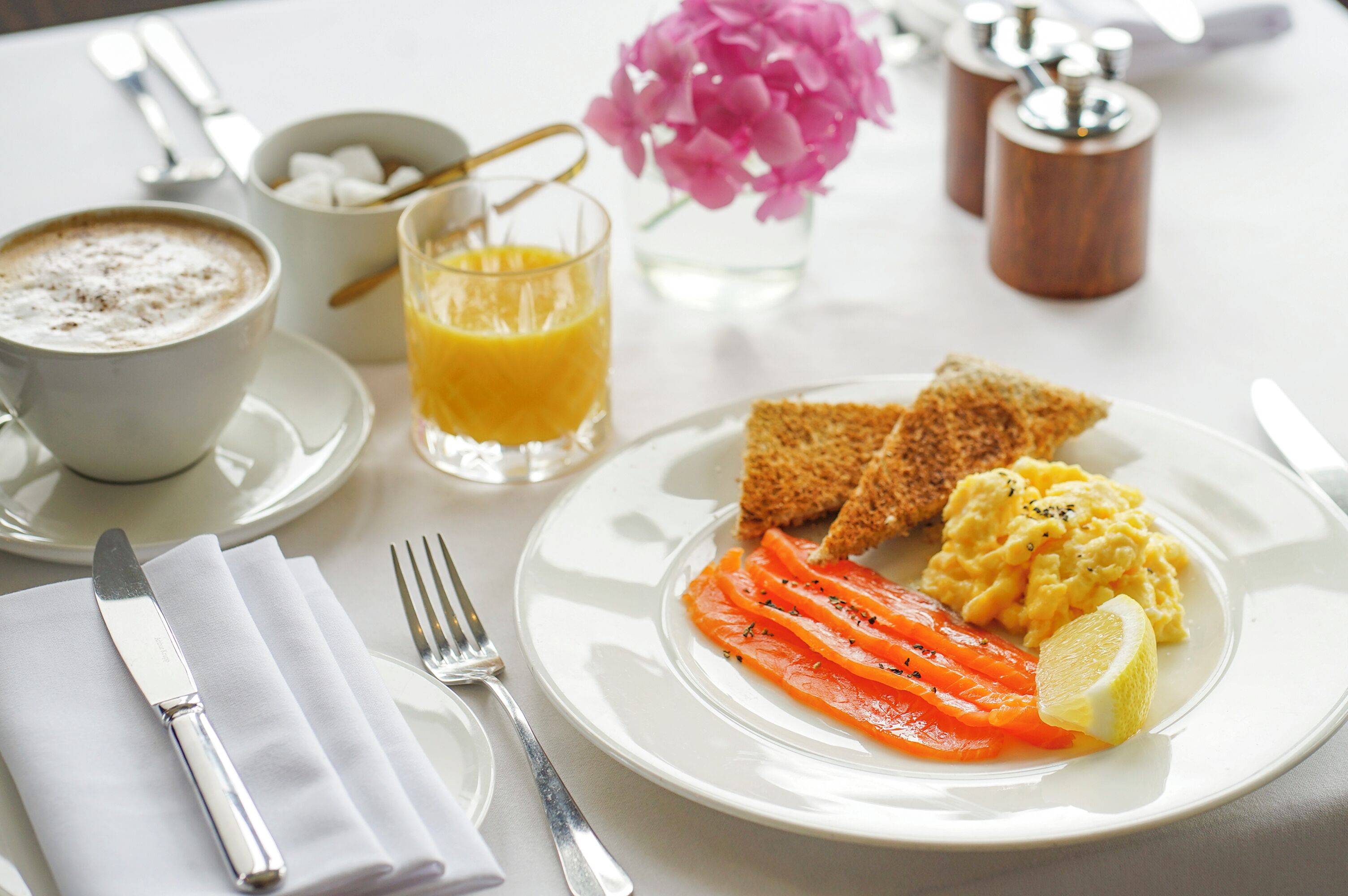 A breakfast setting with toast, scrambled eggs, smoked salmon, and a glass of orange juice on a white plate.
