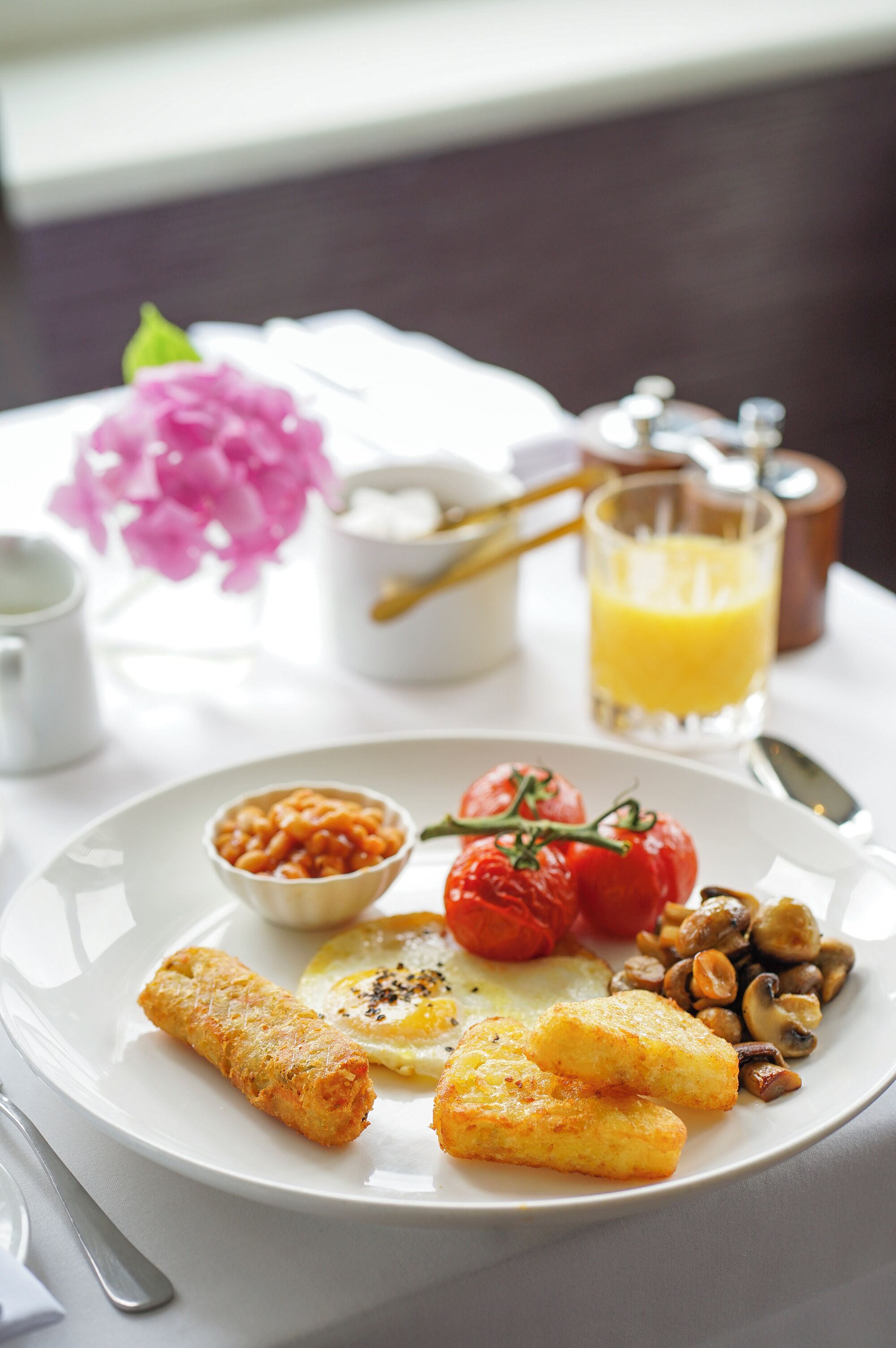 A breakfast plate with eggs, tomatoes, beans, and fried items on a white plate.