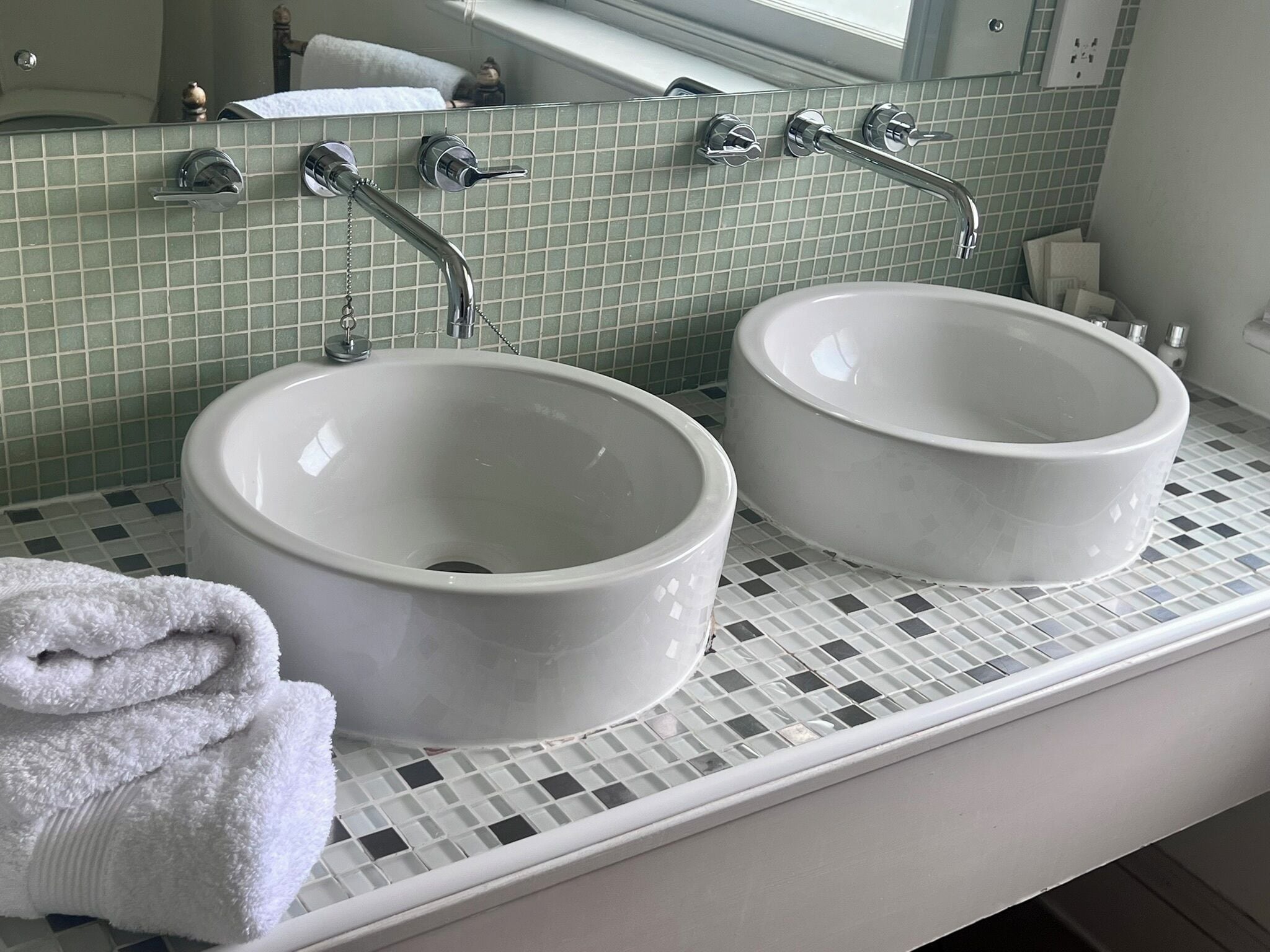 Ein Badezimmer mit zwei weißen Keramikwaschbecken, einem weißen Handtuch und einem Spiegel über den Waschbecken.