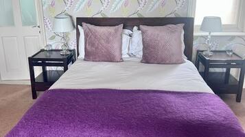 A bedroom with a large bed, two nightstands, a window with blinds, and a floral wallpaper pattern.