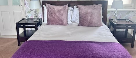A bedroom with a large bed, two nightstands, a window with blinds, and a floral wallpaper pattern.