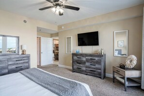 A bedroom with a bed, a ceiling fan, a TV, and a dresser.