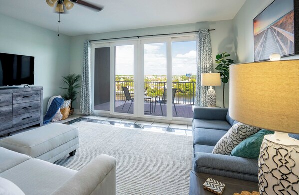 A living room with a sofa, a television, a lamp, and a balcony with a view of the city.