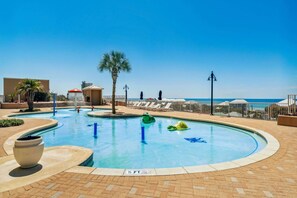 A pool area with a clear view of the ocean, lounge chairs, and a palm tree.