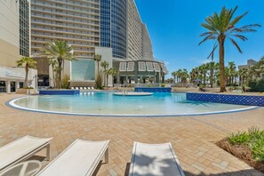 A hotel pool area with lounge chairs, a pool, palm trees, and a building with balconies. - Wharftown Retreat at Laketown Wharf 3BR Condo w/ Balcony Views, Pools, Walk to Beach, Sleeps 8 | Daily Entry to Local Activity Options (Panama City Beach)