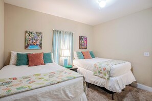 Un dormitorio con dos camas, cada una con cubrecama y almohadas blancas, una ventana con cortinas y un cuadro en la pared.