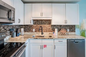 A modern kitchen with white cabinets, a granite countertop, a built-in microwave, and a dishwasher.