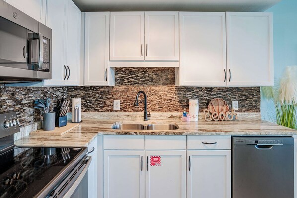 A modern kitchen with white cabinets, a granite countertop, a built-in microwave, and a dishwasher.