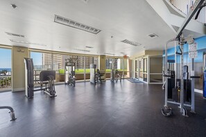 A gym with various exercise equipment, large windows, and a view of buildings.