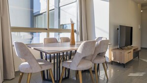A modern dining area with a wooden table and six chairs, a tall vase, and a television on a wooden cabinet. - Elevate - Sleek 2-BR Apt by Santa Maria, Jal el Dib (Jal El Dib)