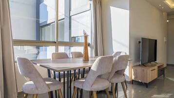 A modern dining area with a wooden table and six chairs, a tall vase, and a television on a wooden cabinet.
