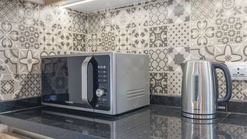 A kitchen with a stainless steel microwave, a kettle, and patterned tiles on the backsplash.