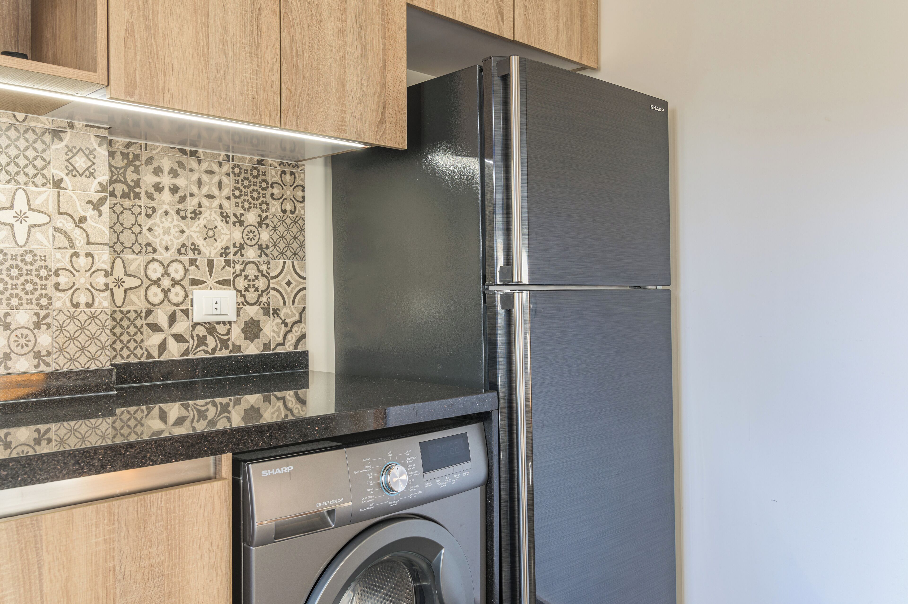 Een keuken met een roestvrijstalen koelkast, een wasmachine en betegelde spatwand.