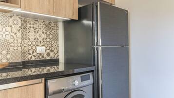 A kitchen with a stainless steel refrigerator, a washing machine, and patterned backsplash tiles.