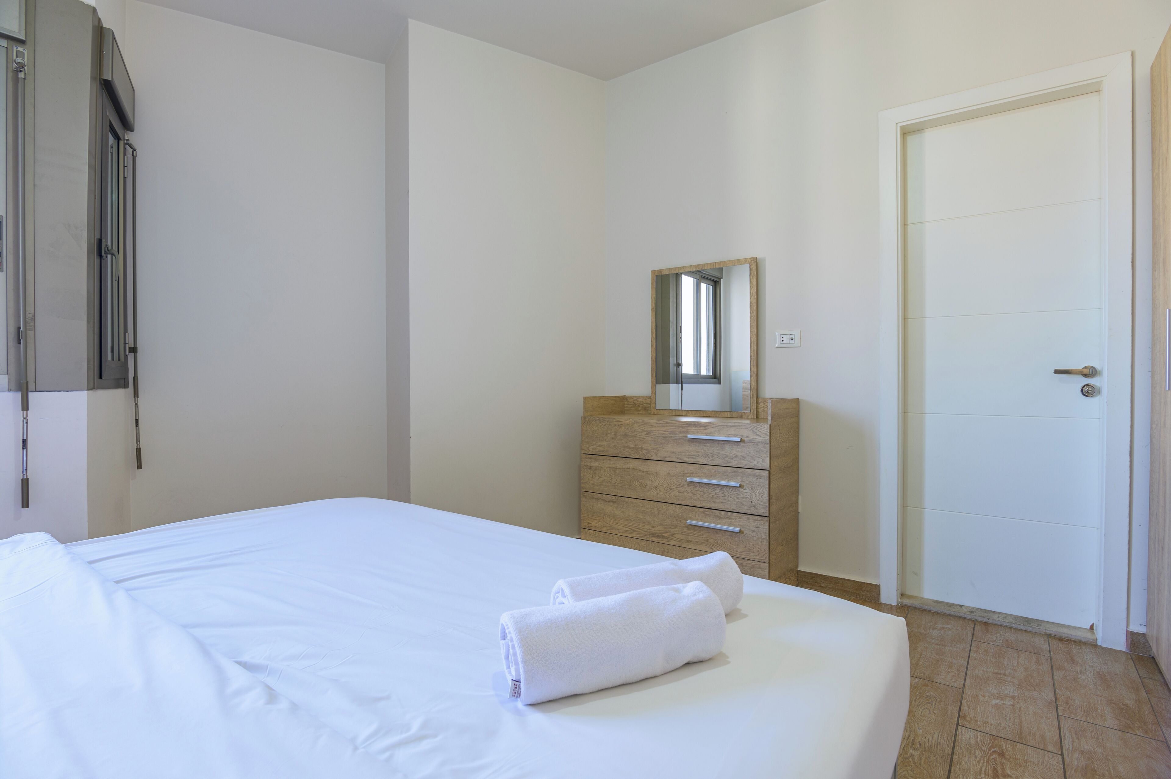 A hotel room with a bed, a wooden dresser, a mirror, and a door.
