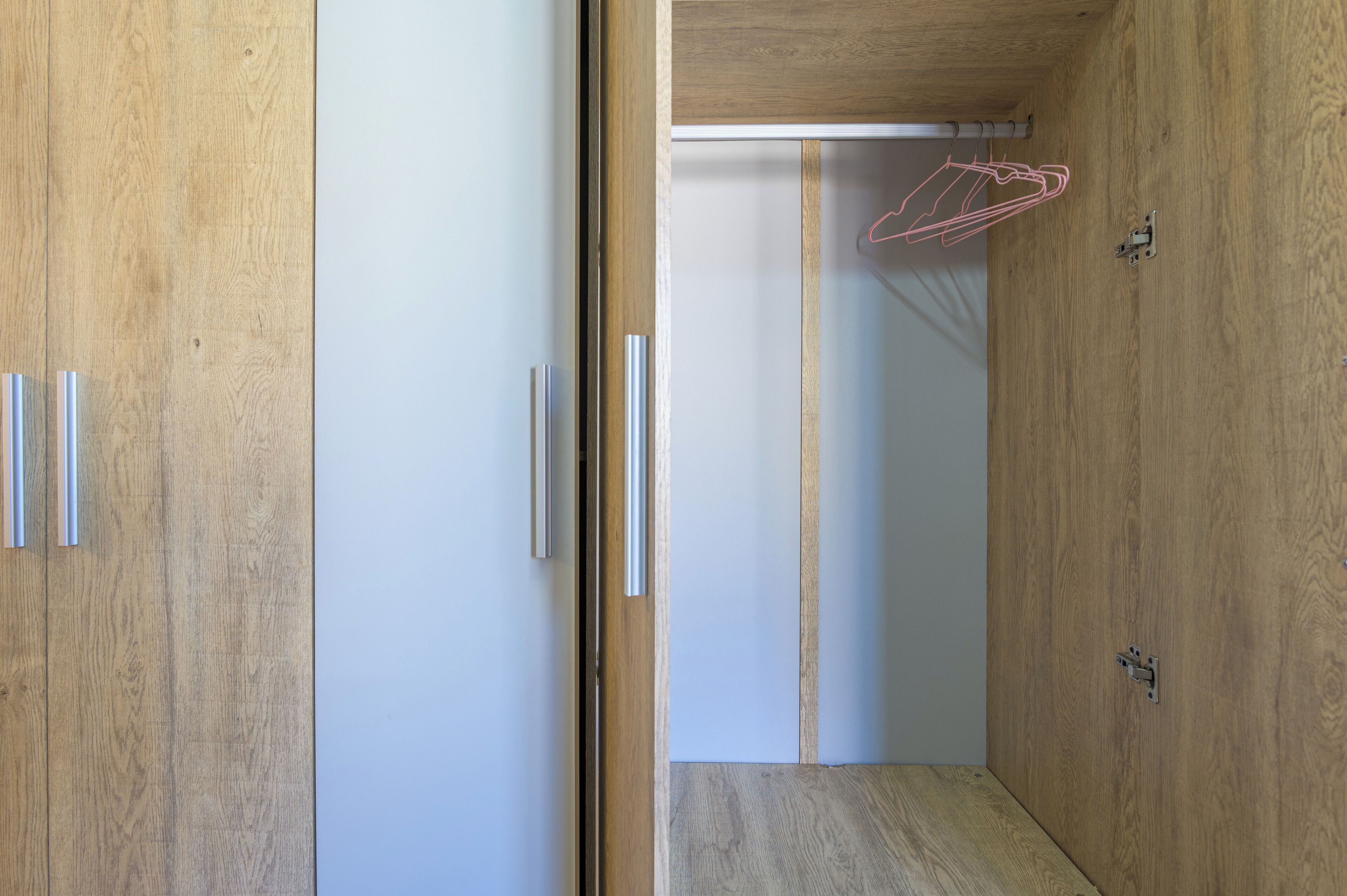 A room with wooden flooring, a white door, and a wooden wardrobe with a hanging rack.