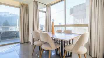 A modern dining area with a rectangular table and six chairs, large windows with curtains, and a view of the cityscape.