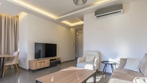 A modern living room with a flat-screen TV, a sofa, a coffee table, and a dining area with chairs. - Elevate - Sleek 2-BR Apt by Santa Maria, Jal el Dib (Jal El Dib)