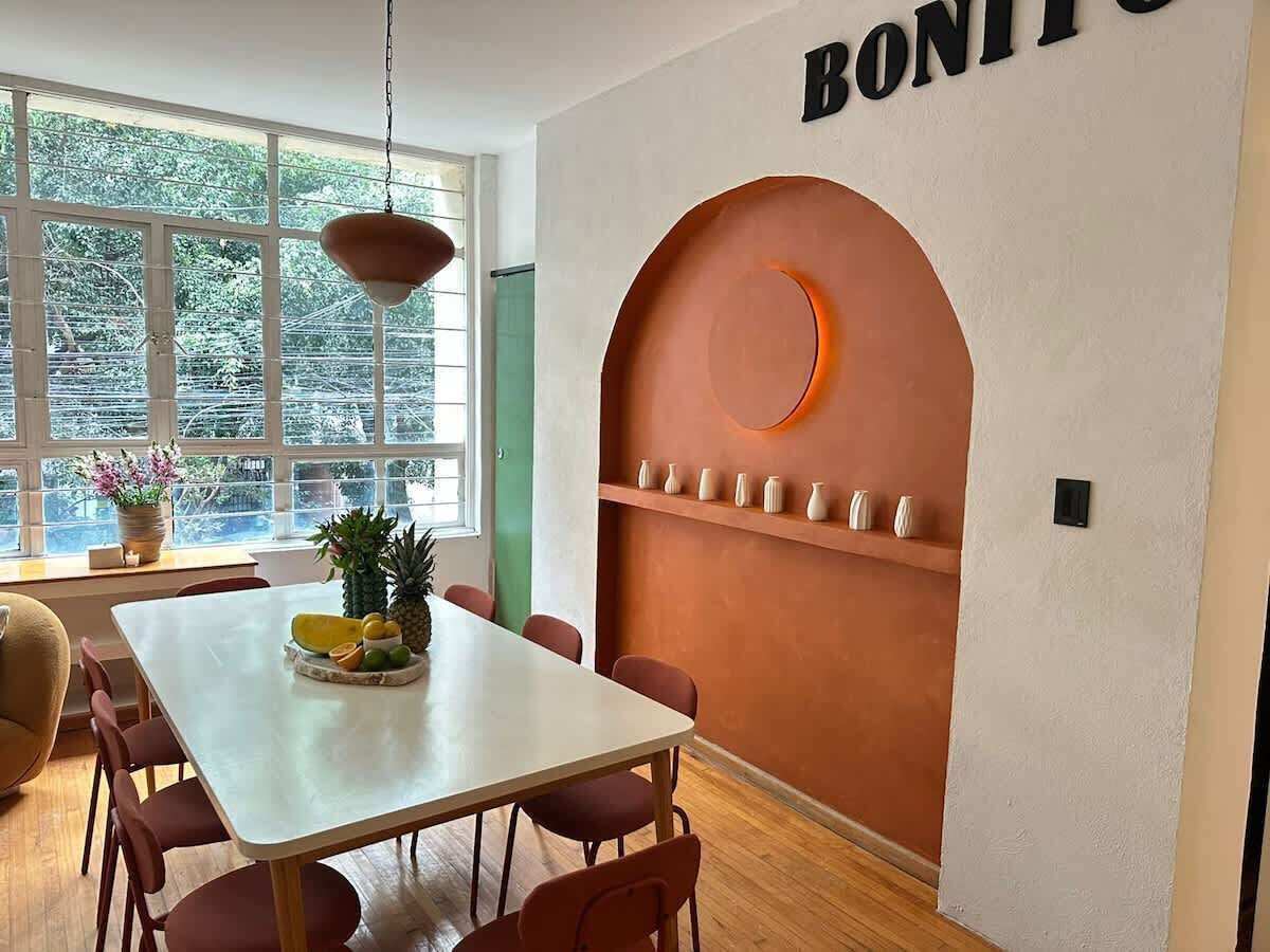 Ein Essbereich mit einem weißen Tisch, roten Stühlen, einer Obstschale und einer Wand mit einem kreisförmigen Design und Regalen.