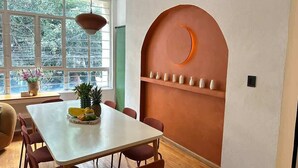 Ein Essbereich mit einem weißen Tisch, roten Stühlen, einer Obstschale und einer Wand mit einem kreisförmigen Design und Regalen.