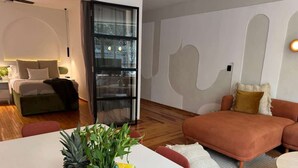 Ein modernes Wohnzimmer mit einem weißen Esstisch, einer Couch und einem Couchtisch. Auf dem Tisch befinden sich eine Ananas und eine Wassermelone.