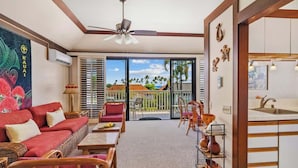 A spacious living area with a red sofa, wooden chairs, a dining table, and a kitchen area with a sink and cabinets.