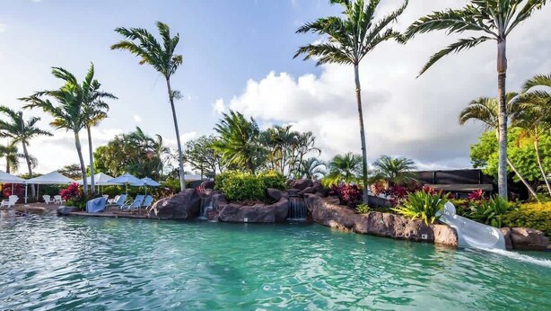 A pool area with clear water, palm trees, and lounge chairs.