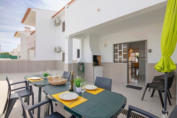 An outdoor dining area with a table set for two, chairs, and a bright yellow umbrella.