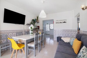 A modern living room with a dining area, a flat-screen TV, and a sofa with cushions.