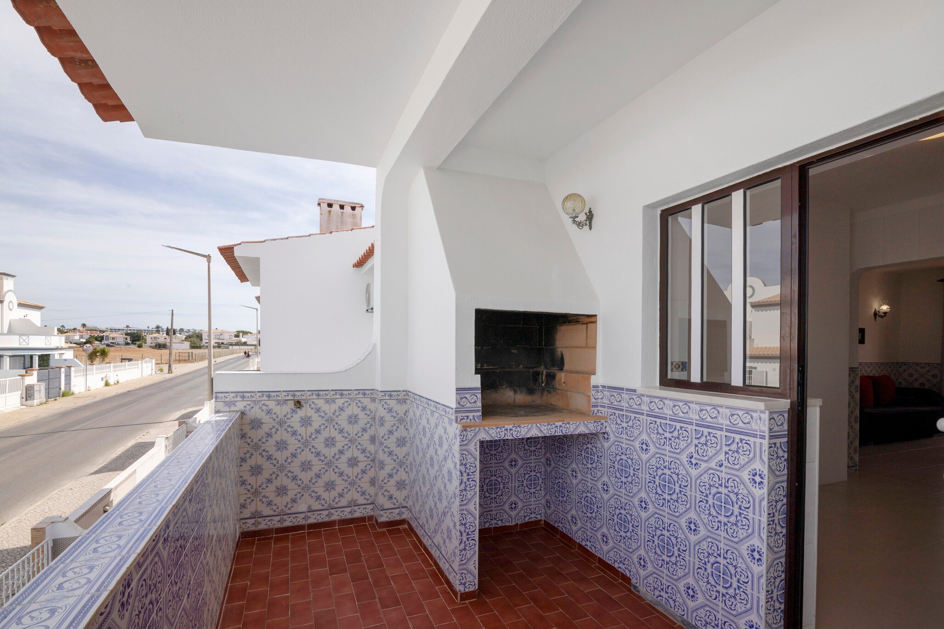 A balcony with patterned tiles, a built-in grill, and a view of the street.