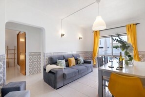 A living room with a sofa, a dining table, yellow curtains, and a window with a view.