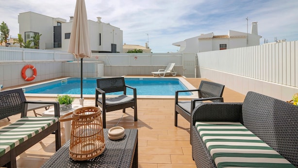 Un espace piscine aménagé sur le toit, avec des chaises longues, une table en osier et une clôture blanche.