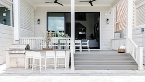 A covered outdoor area with a pool, white chairs, and a grill. - The 1300 | 4 Home Combo, 28 bedrooms | Heated Pool (New Orleans)