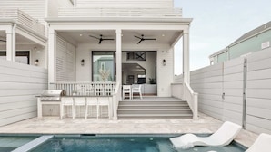 A modern house with a pool, a covered patio with white furniture, and a staircase leading to the interior. - The 1300 | 4 Home Combo, 28 bedrooms | Heated Pool (New Orleans)