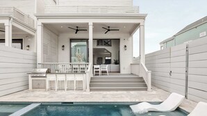 A modern house with a pool, a covered patio with white furniture, and a staircase leading to the interior. - The 1300 | 4 Home Combo, 28 bedrooms | Heated Pool (New Orleans)